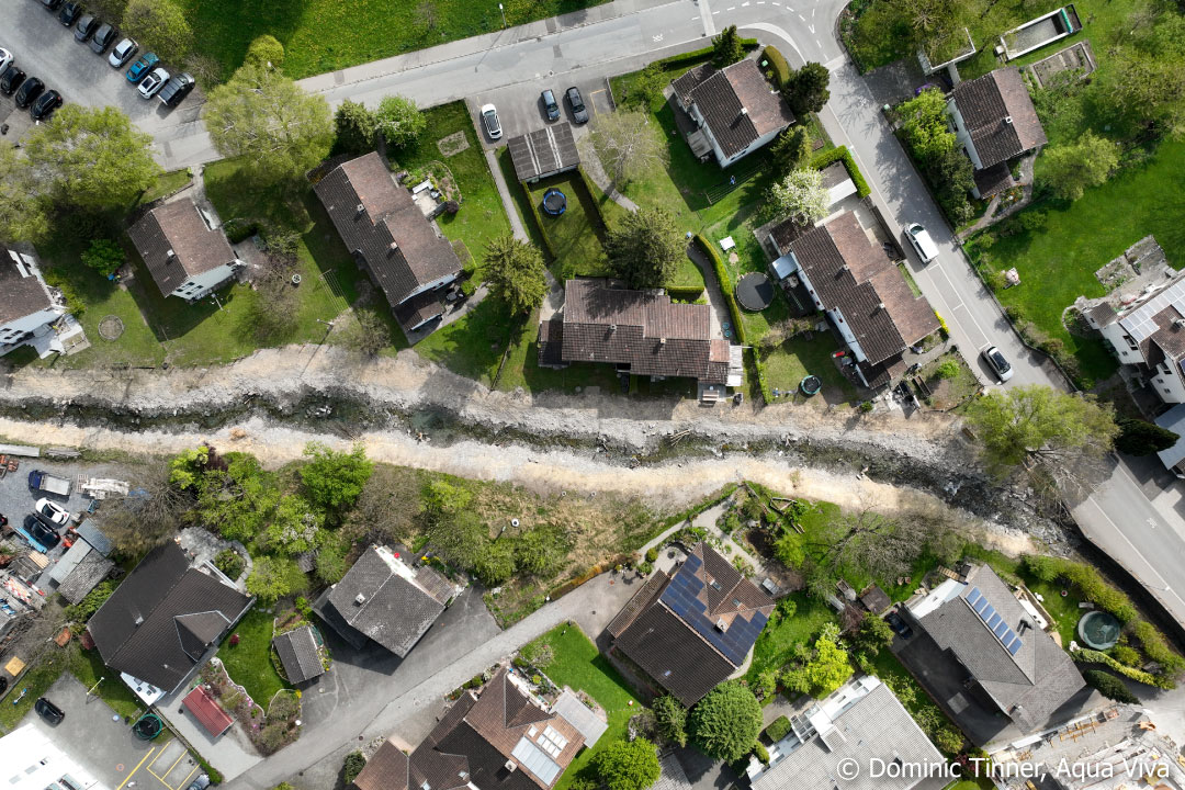 Luftaufnahme vom revitalisierten Sevelerbach mit unbewachsenem Ufer zwischen Häusern
