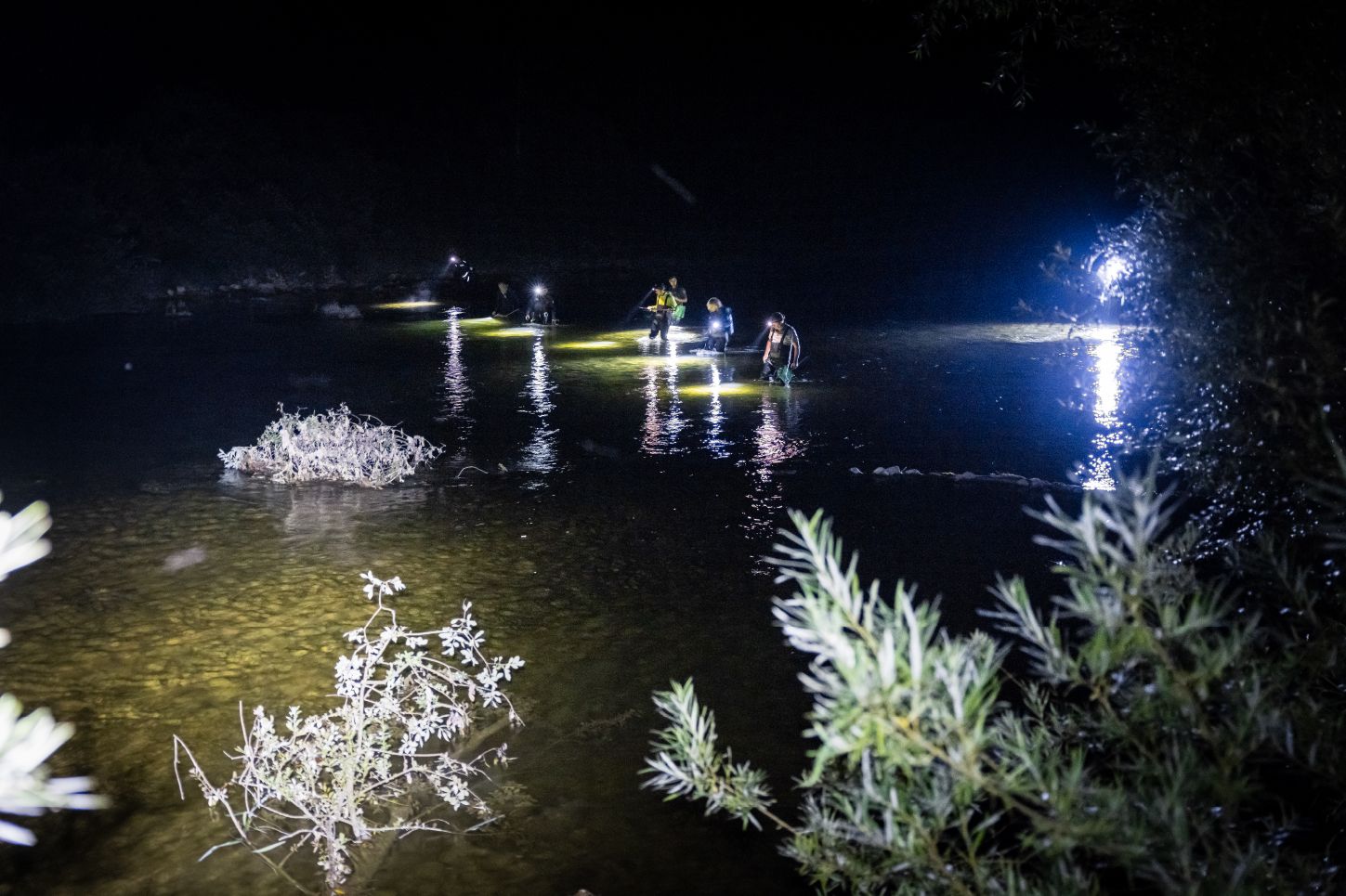 Nachtaufnahme von einem Fluss, in dem mehrere Menschen mit Taschenlampe gehen.
