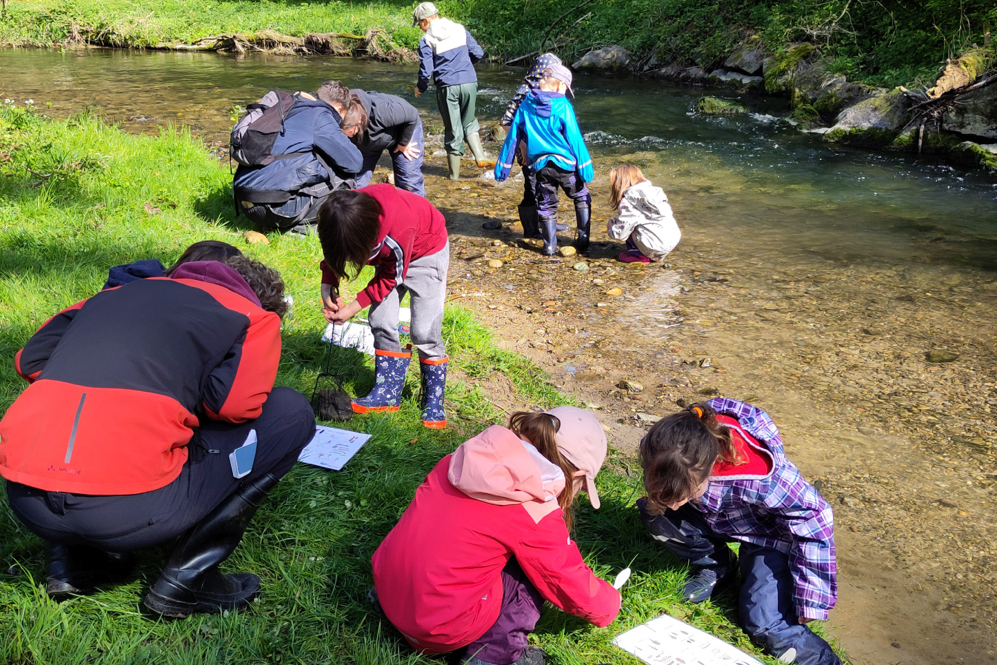 Kinder vermessen die Breite von einem Bach mit Massband.