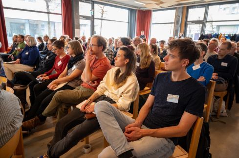 Menschen im Publikum auf Stühlen, die nach vorne schauen.