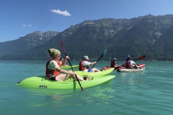 Kajak-Fahrer:innen auf einem türkisblauen See mit Bergen im Hintergrund